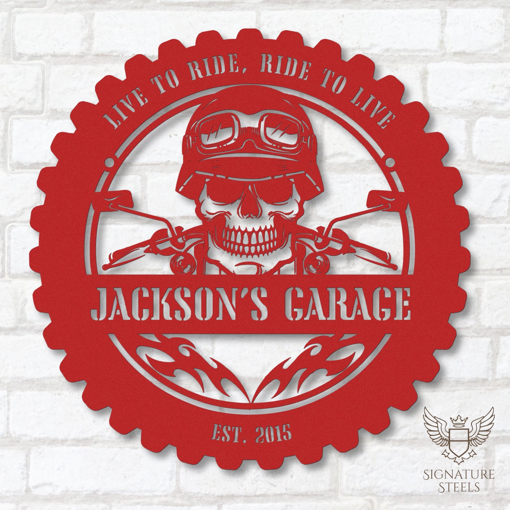 A round red metal sign for a garage or man's cave with a frame imitating a motorcycle tyre, a skull wearing a biker's helmet over a motocycle handlebar and flames in the centre. The sign says 'Live to ride, ride to live", 'Jackson's Garage' and 'Est. 2015', hanging on a white brick wall.