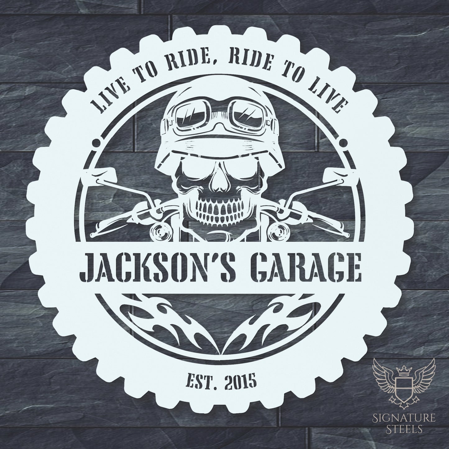 A round white metal sign for a garage or man's cave with a frame imitating a motorcycle tyre, a skull wearing a biker's helmet over a motocycle handlebar and flames in the centre. The sign says 'Live to ride, ride to live", 'Jackson's Garage' and 'Est. 2015', hanging on a dark grey brick wall.
