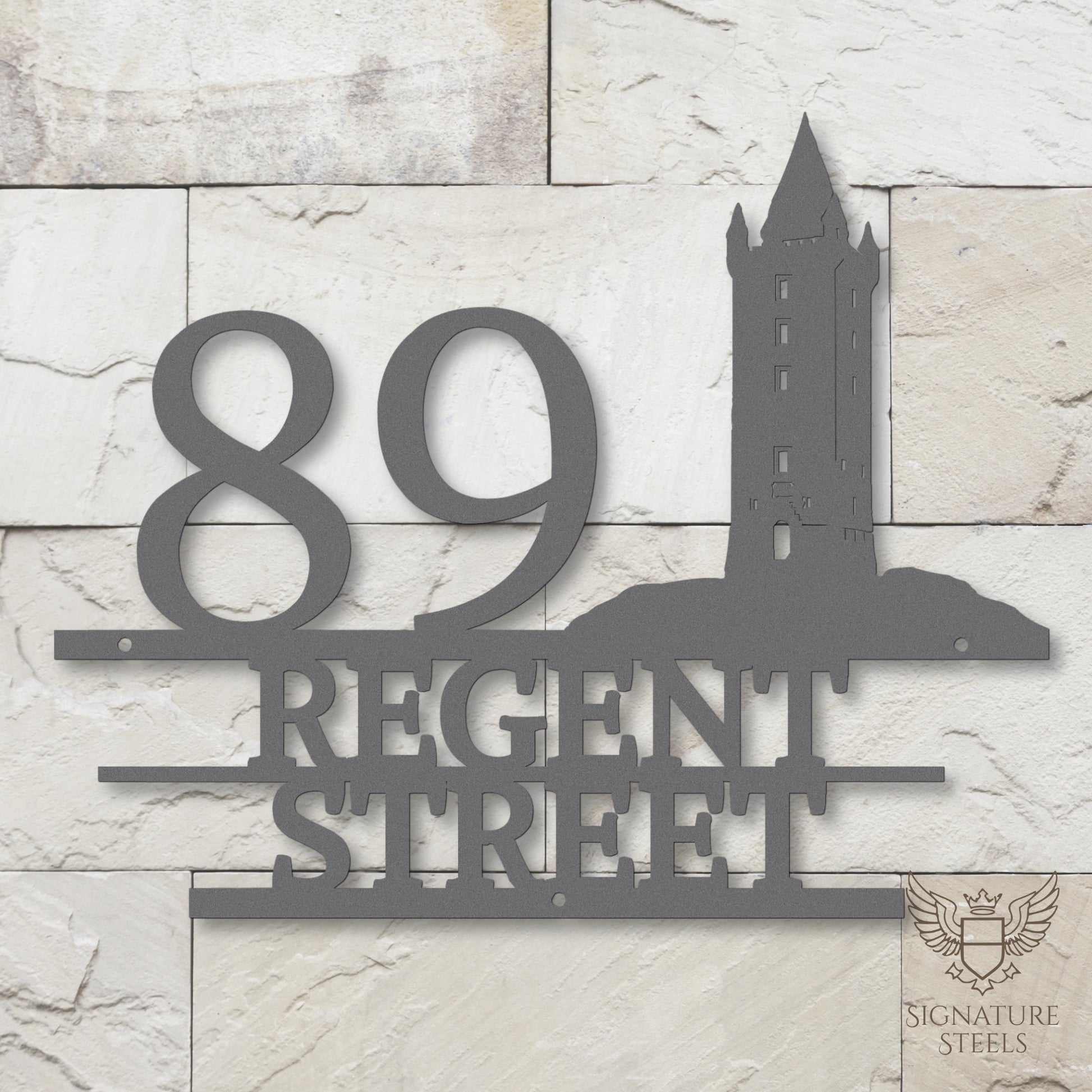 Silver metal address sign with house number 89, street name Regent Street, horizontal parallel lines and a silhouette of Scrabo Tower, a landmark of Newtownards in Northern Ireland, hanging on a white and beige brick wall.